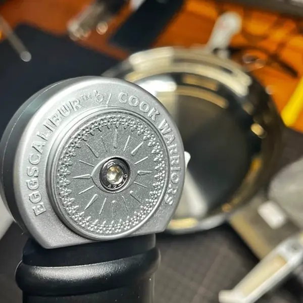 Eggscalibur pommel close-up — laser-engraved 'Eggscalibur by Cook Warriors' medallion on the smart stainless steel sword pan